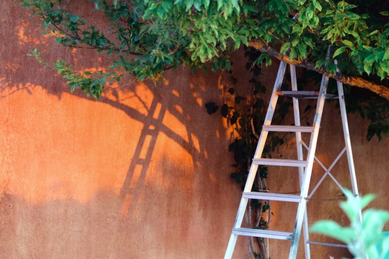 A person standing on a ladder cleaning leaves from the gutter of a residential house.