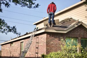 A family moves outdoor furniture away from a house while roofing materials are stacked nearby.