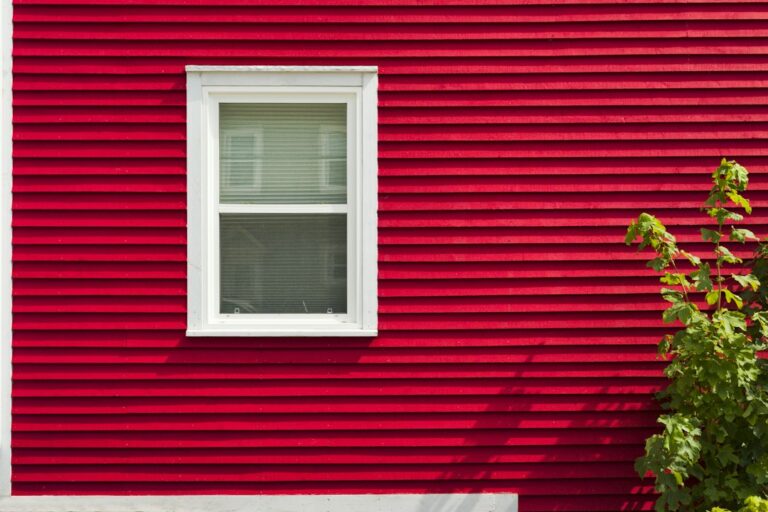 House exterior showing stucco and vinyl siding sections after light rain, with windows, trim, and drainage details visible
